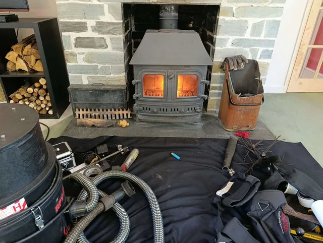 Dust sheets, vacuum and sweeping kit laid out in front of a stove in a slate fireplace