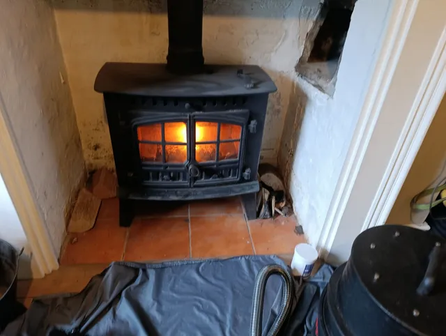 A swept wood burner lit in a whitewashed fireplace